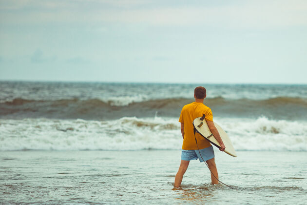大海一个男人拿着冲浪板站在海滩上微笑冲浪自然