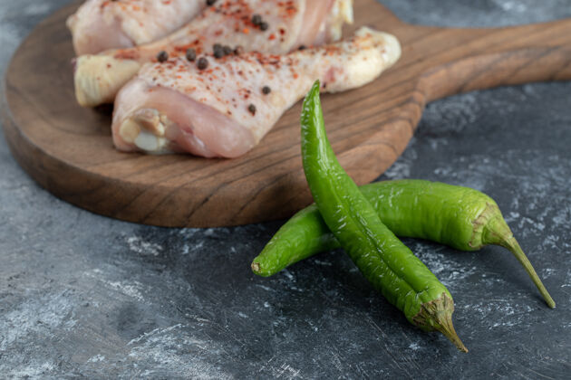 深色绿色辣椒和生鸡腿的特写照片在灰色背景上柠檬准备鸡肉