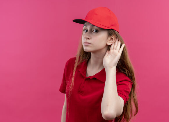 女人穿着红色制服的年轻送货员在隔离的粉色墙壁上做着听不见你说话的事女孩分娩制服