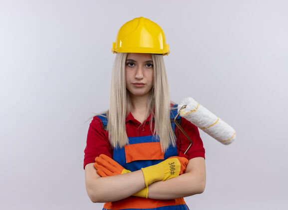 拿着年轻的金发碧眼的建筑工女孩 穿着制服 戴着手套 拿着油漆辊 站在封闭的位置上 看着隔离的白色墙壁和复印空间油漆工金发工程师