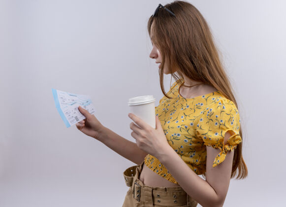 视图年轻的旅行女孩头戴太阳镜 拿着飞机票和塑料咖啡杯 站在隔离的白色墙壁上看侧面图中的票咖啡票头