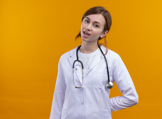 穿疲惫的年轻女医生穿着医用长袍 手持听诊器 将手放在背上 放在隔离的橙色墙上 留有复印空间女人医生女人