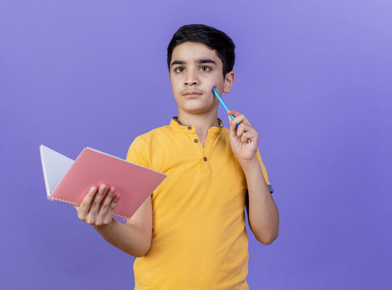 年轻人体贴的年轻白人男孩拿着便笺簿 用铅笔触摸脸颊 看着紫色墙壁上孤立的一面 留着复印空间铅笔表达男人