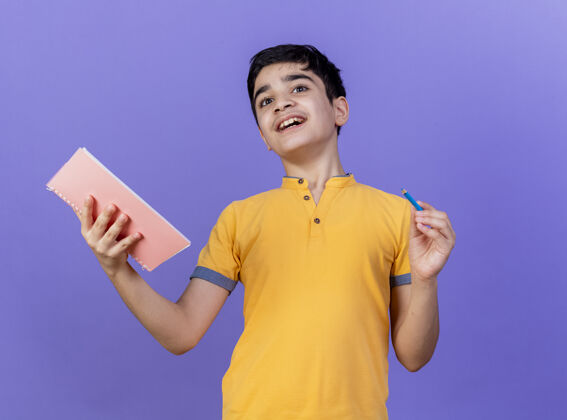 男孩令人印象深刻的年轻白人男孩拿着笔记本和铅笔孤立在紫色的墙上手势男人年轻人