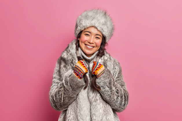 女士穿着冬装的北极女人微笑着生活在寒冷的气候微笑着轻轻地把辫子隔离在粉红色的墙上请漂亮节日