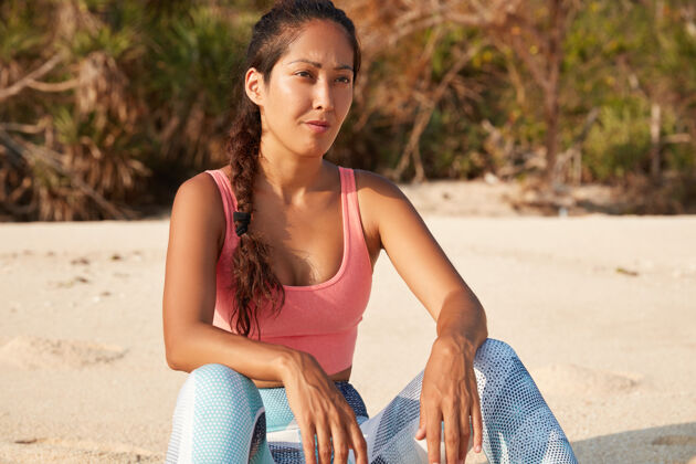 健康穿着运动服的年轻女性慢跑者感觉健康 若有所思地看着远处 在沙滩上摆姿势锻炼慢跑日落