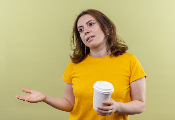 杯子年轻随意的女人拿着塑料咖啡杯 在孤立的绿色墙壁上空手看着左边壁板持有女人