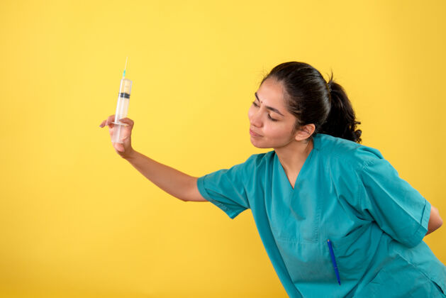 成人黄色墙上拿着注射器的年轻女医生的正视图年轻女医生人快乐
