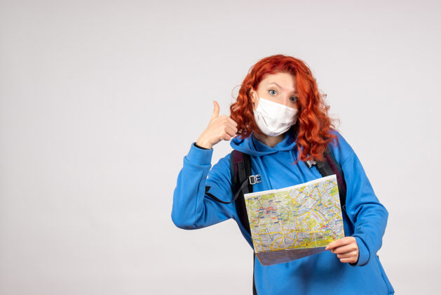 地图前视图的年轻女性与背包和地图在面具上的白色墙壁成人背包微笑