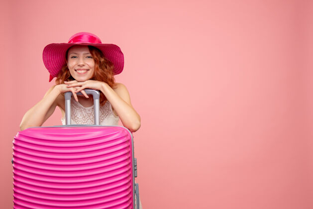假期年轻的女性游客与粉红色的帽子和粉红色的墙壁上的包的正面视图时尚微笑情感