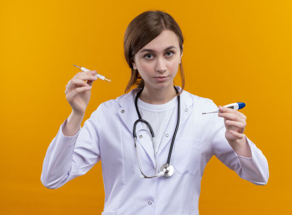 养着体贴的年轻女医生 穿着医用长袍 戴着听诊器 用手指举着温度计 站在隔离的橙色墙上 留着复印空间戴着女人女人