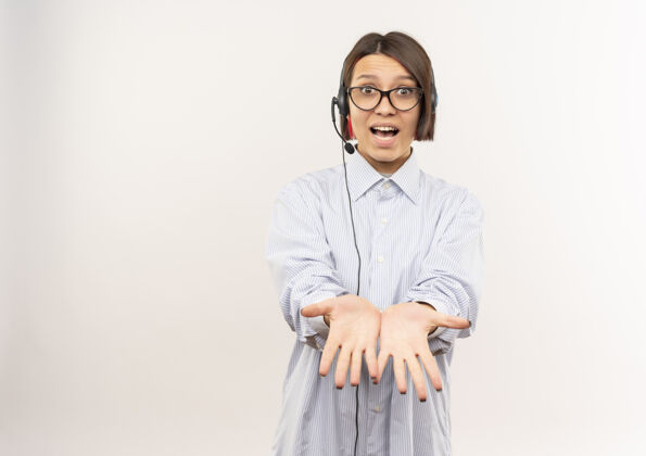伸展令人印象深刻的年轻呼叫中心女孩戴着眼镜和耳机伸出双手显示空手孤立在白色的复印空间电话显示手