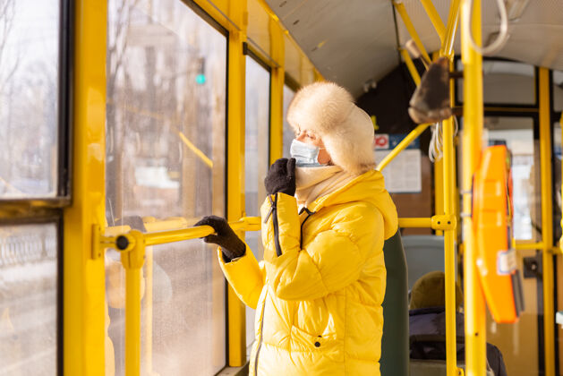 温暖一个穿着暖和衣服的年轻女子在一个冬天的城市公共汽车上的明亮的阳光肖像防护面罩地铁检疫