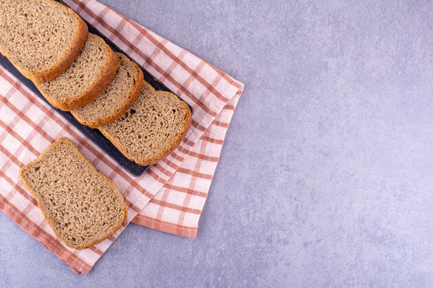 饮食在大理石表面的折叠毛巾上放一盘黑色的棕色切片面包口味营养切片