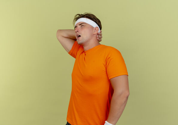 站立疼痛的年轻英俊的运动型男子戴着头带和腕带站在侧视图把手放在脖子后面看起来笔直孤立在橄榄绿与复制空间年轻空间轮廓
