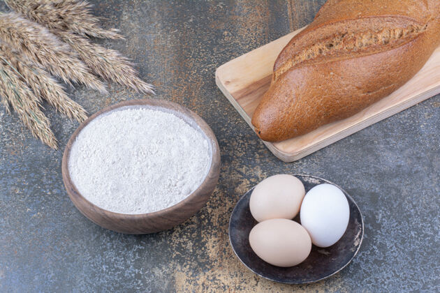 配料接力棒面包旁边的一块板麦秆面粉碗和鸡蛋大理石表面芝麻烘焙面粉