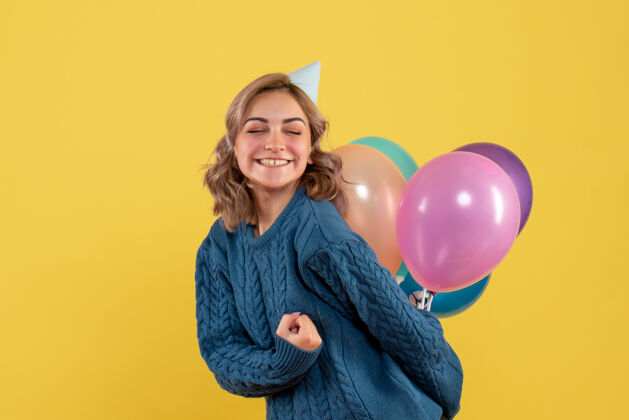 飞机年轻的女性把五颜六色的气球藏在黄色的背上气球生日视图