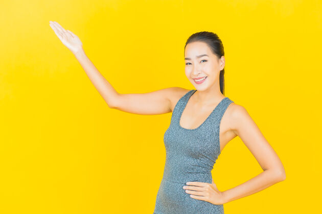 欢呼在黄色的墙上 描绘一位穿着运动服准备锻炼的美丽亚洲年轻女子穿着运动放松