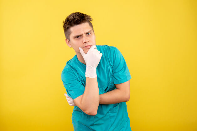 背景正面图：年轻的男医生 穿着医疗服 戴着手套 在黄色背景下思考人手套肖像