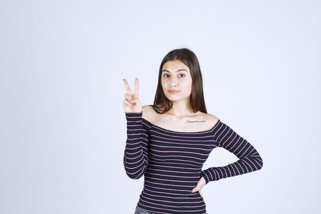女人穿条纹衬衫的年轻女子发出和平信号信息模型积极