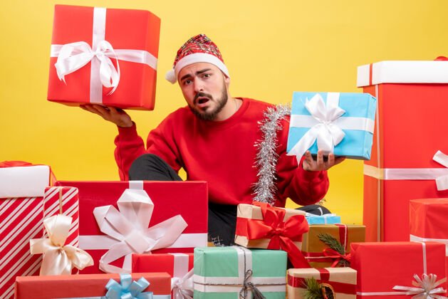 礼物正面图：年轻男性围坐在黄色背景上的圣诞礼物旁丝带礼物年份