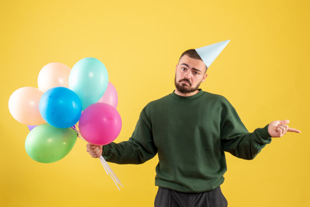 快乐正面图黄色背景上有彩色气球的年轻男性庆祝生日一年