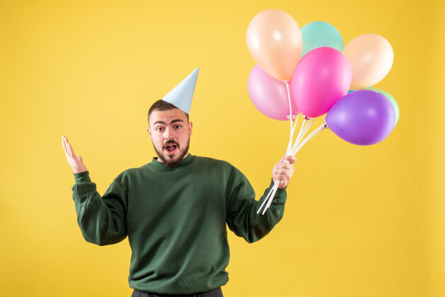 庆祝正面图黄色背景上手持彩色气球的年轻男性空气年轻的男性背景
