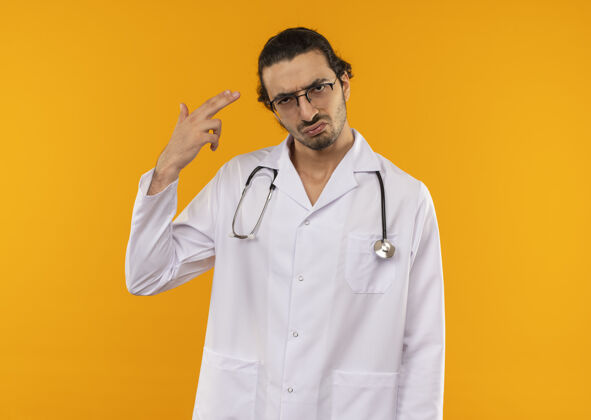 医生悲伤的年轻医生戴着医用眼镜 穿着医用长袍 听诊器在隔离的黄色墙上显示着的手势 还有复印空间长袍眼镜年轻