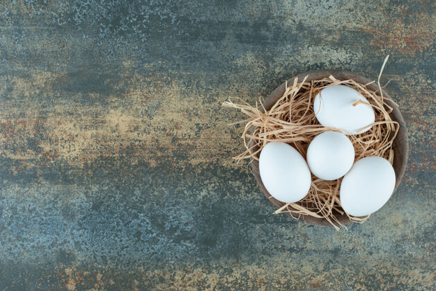 未经烹调的新鲜的鸡蛋躺在干草木碗上生的白有机