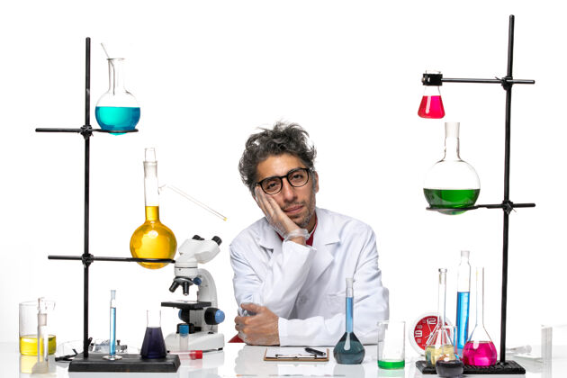 解决方案前视图穿着白色医疗服的男科学家坐在桌子前 带着解决方案桌子实验室外套科学