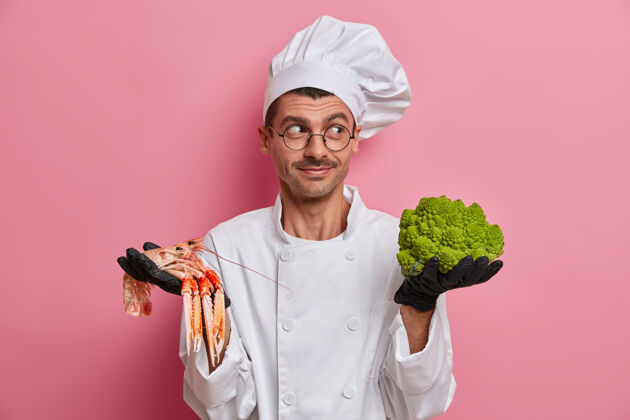 眼镜面带微笑的厨师高兴地站在一边 戴着厨师帽 穿着制服 拿着绿花椰菜 鱼 建议咖啡馆素食者的最佳菜单眼镜营养忙碌