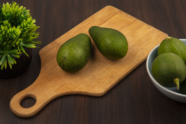 膳食新鲜的绿色鳄梨在木制厨房板上的顶视图 在木制墙上的碗上放着酸橙美食小吃碗