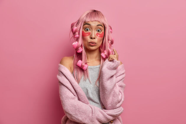 光滑惊讶的亚洲女人 粉色头发 在早高峰时使用卷发器 胶原蛋白贴片 接受美容治疗滚轴粉色假发人类