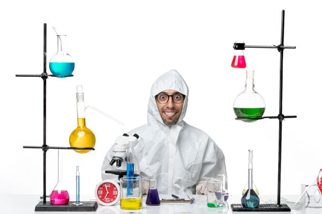 罐子正面图穿着特殊防护服的男科学家围坐在办公桌旁 拿着解决方案玻璃坐着实验室