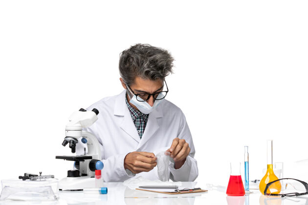 化学正面图中年科学家穿着特制的西装 戴着面具围坐在桌子旁 拿着解决方案科学技术人员解决方案