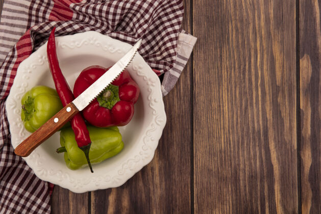 刀顶视图新鲜的铃铛和辣椒在一个碗在一个格子布与刀在一个木墙上复制空间用餐检查菜肴