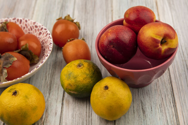 橘子一个碗上的多汁的软桃子的俯视图 灰色的木墙上孤立着柿子和橘子多汁碗新鲜