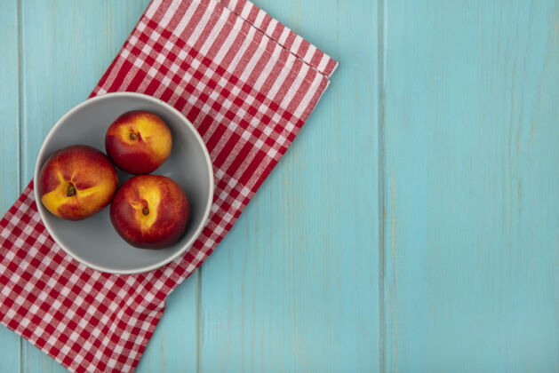 观点一个碗上新鲜多汁的桃子的俯视图 在蓝色的木墙上有一块红色格子布 上面有复制空间新鲜桃食品