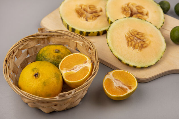 饮食在灰色墙壁上的桶上的木制厨房板上隔离着蜜瓜片和蜜瓜的顶视图橘子厨房木头