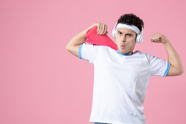 视野正面图：穿着运动服的年轻男性 粉色墙上有瑜伽垫和耳机人物水平年轻男性