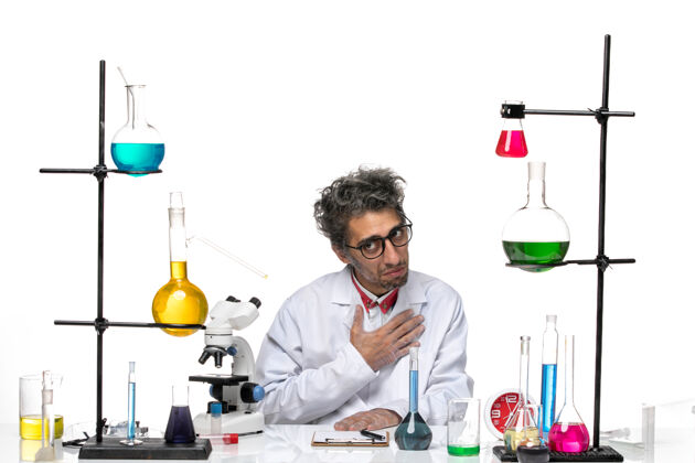 解决方案前视图穿着白色医疗服的男科学家坐在桌子前 带着解决方案化学实验室专业