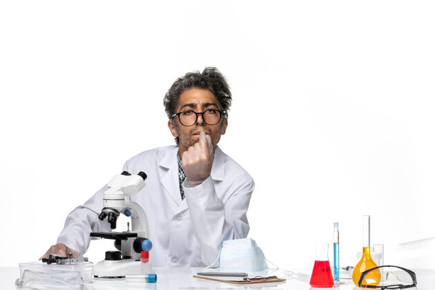 专业正面图身着特殊套装的中年科学家围坐在桌子旁 拿着显微镜和溶液周围实验室显微镜