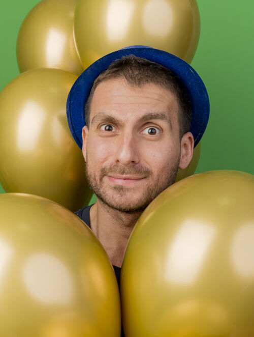 党一个戴着蓝色派对帽的帅哥拿着氦气球望着绿色墙壁上孤立的前方举行人气球