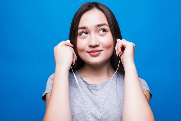 欢呼戴着耳机听音乐的亚洲女人被隔离在蓝色的墙上女性手机耳机