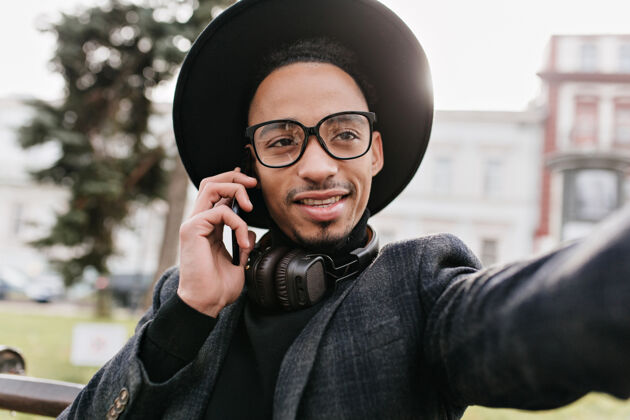 快乐戴着耳机的黑眼睛男人在公园里自拍时髦的非洲男人一边给别人打电话 一边给自己拍照手机城市情感