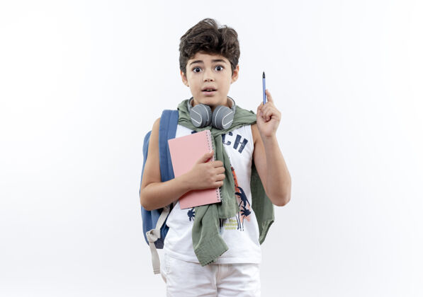手势惊讶的小男生背着书包 戴着耳机 拿着笔记本 举着笔 孤零零地站在白纸上握着表情小