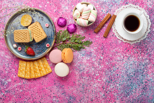 食物俯瞰美味的华夫饼 麦卡龙和粉红色表面上的一杯茶麦卡龙生的洗漱用品