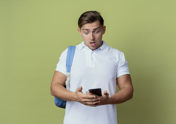 年轻惊讶的年轻帅气的男生背着书包拿着手机看着橄榄绿上的孤零零学生包绿色