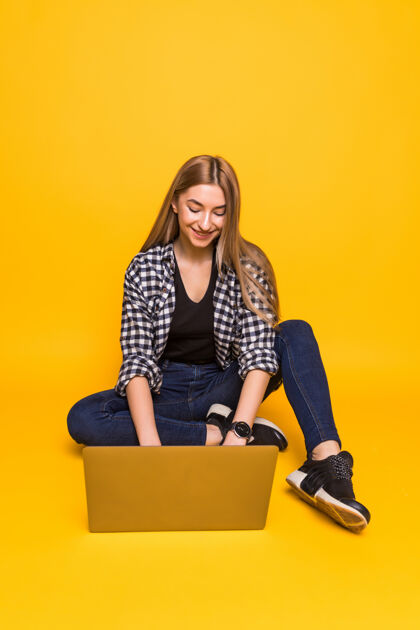 休闲坐在地板上微笑的年轻女子 笔记本电脑被隔离在黄色的墙上自由职业者学生欢呼