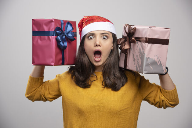 肖像戴圣诞帽的年轻女子手里拿着礼品盒惊喜快乐礼品盒
